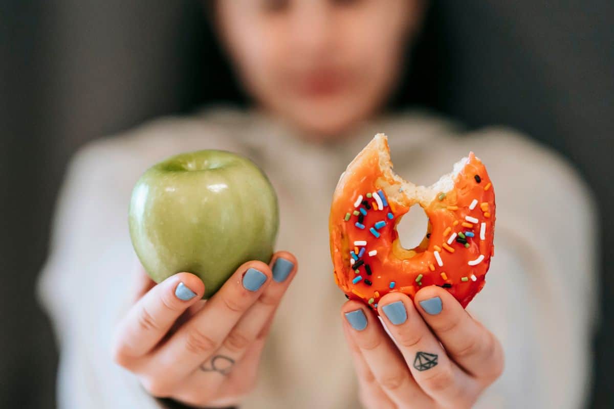 Hand holding a green apple and a sprinkled donut