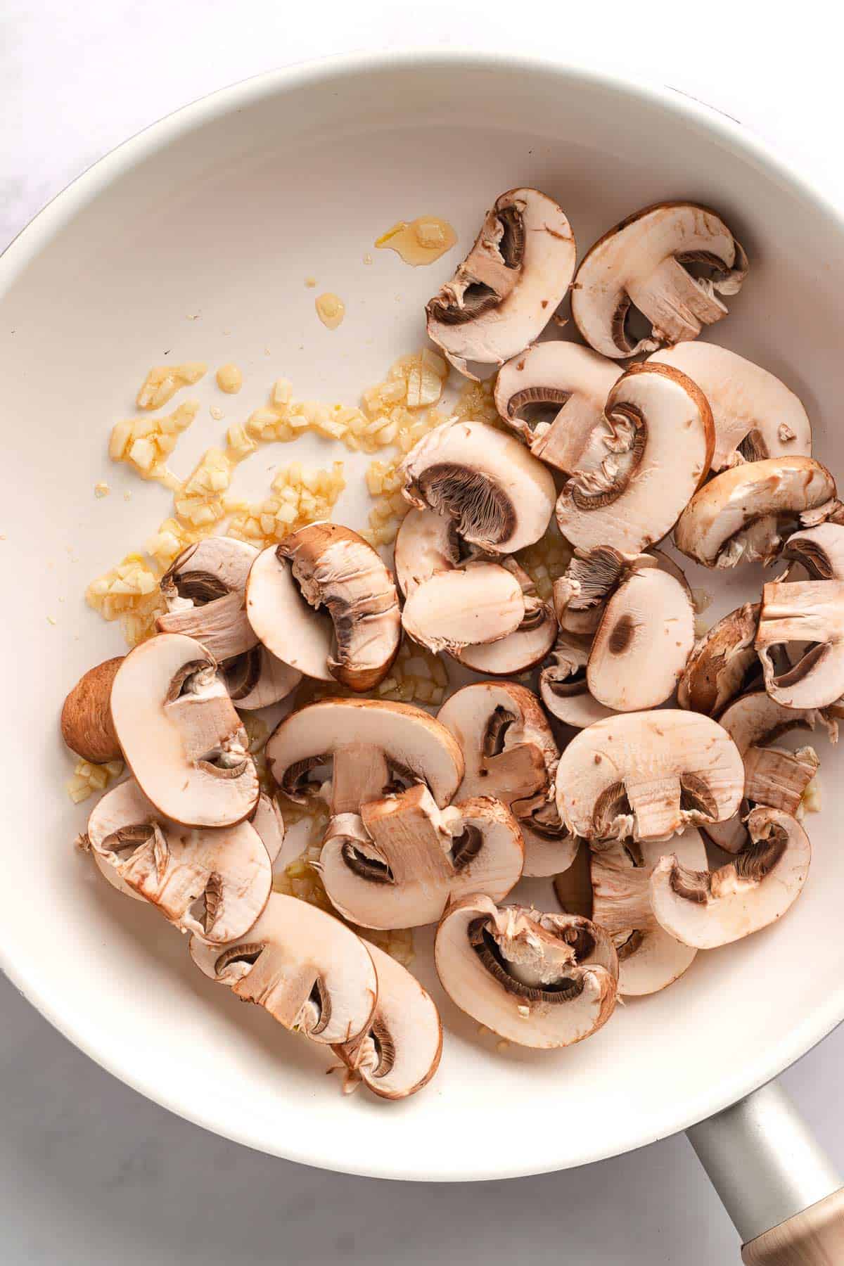 Sliced mushrooms added to a skillet with sautéed garlic.