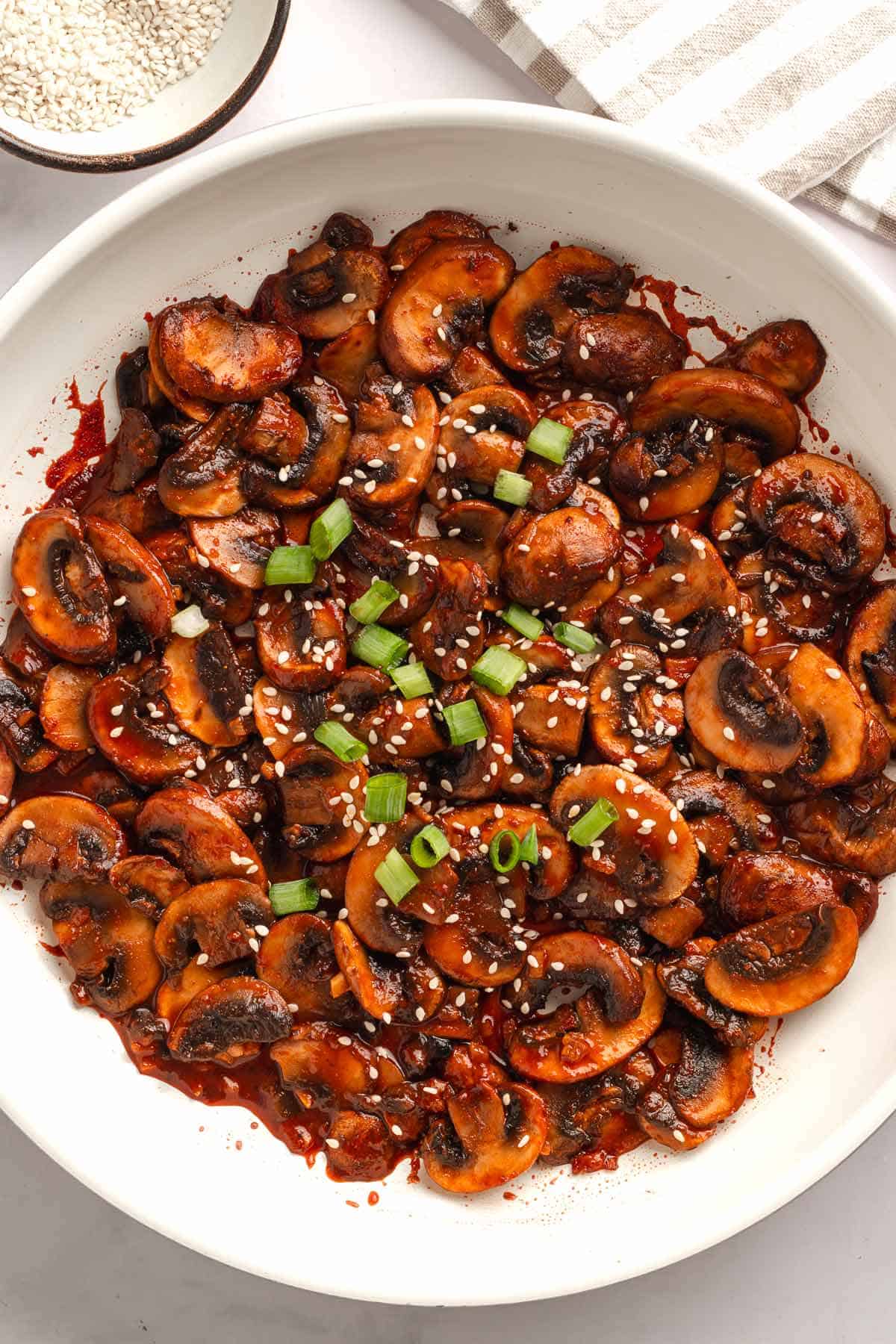 Vegan spicy sauteed mushrooms in a skillet topped with sesame seeds and green onions.