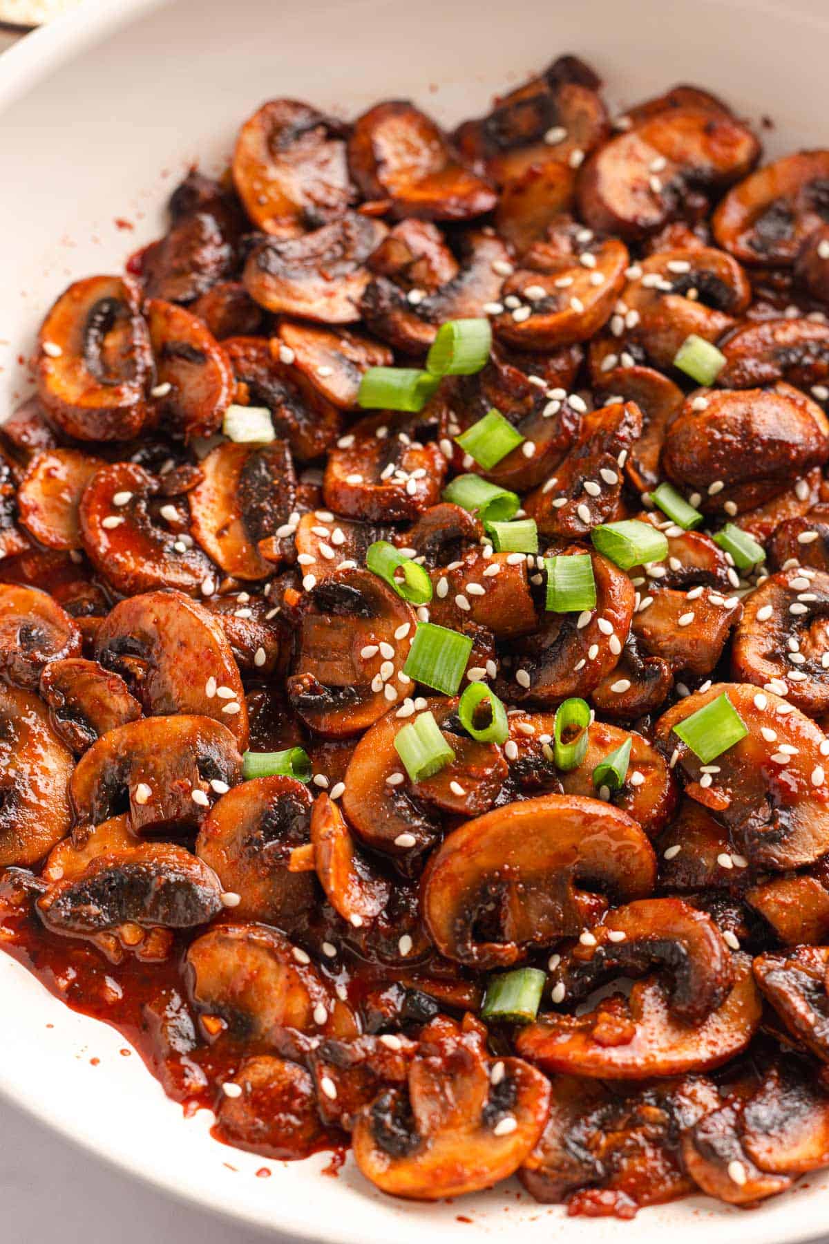 Close-up of spicy sauteed mushrooms garnished with sesame seeds and green onions.