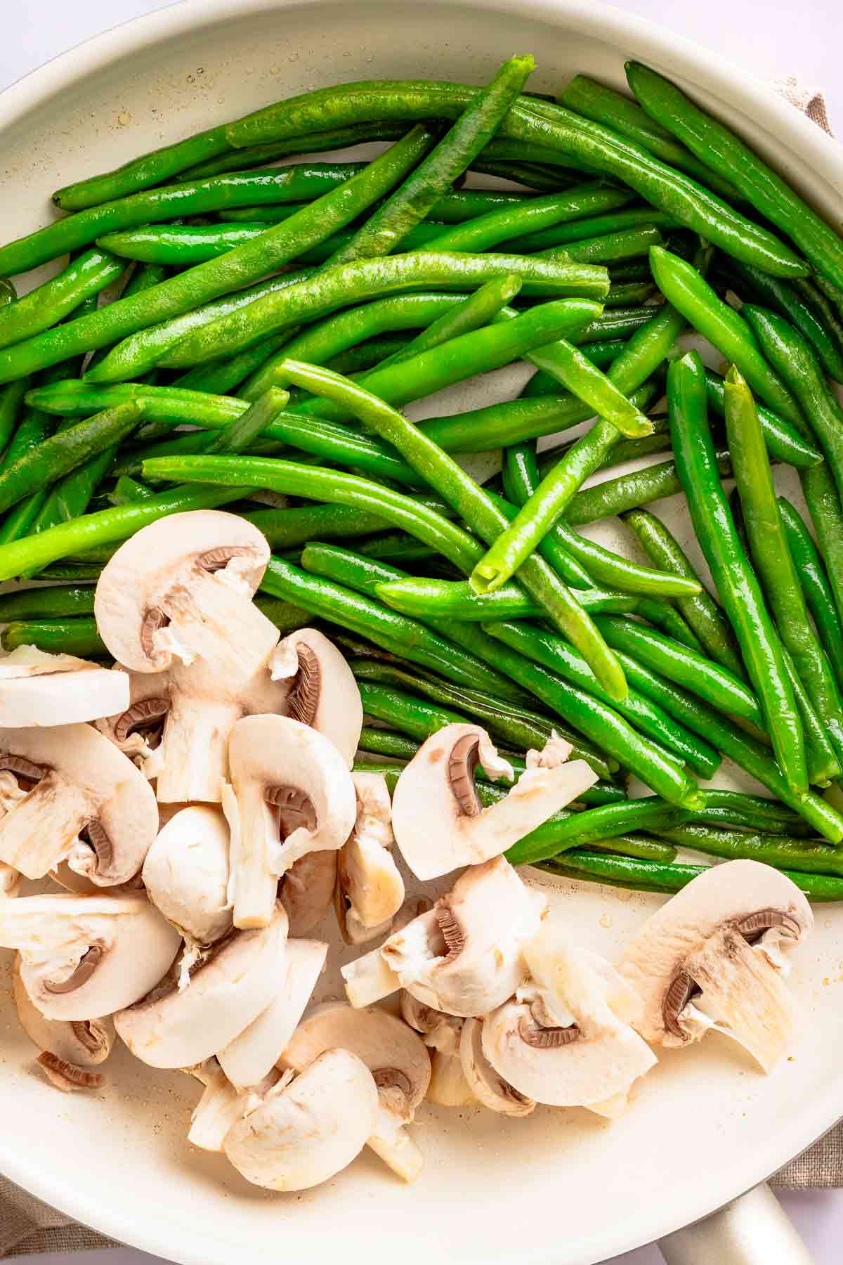 Sliced mushrooms added to green beans in a skillet before cooking together