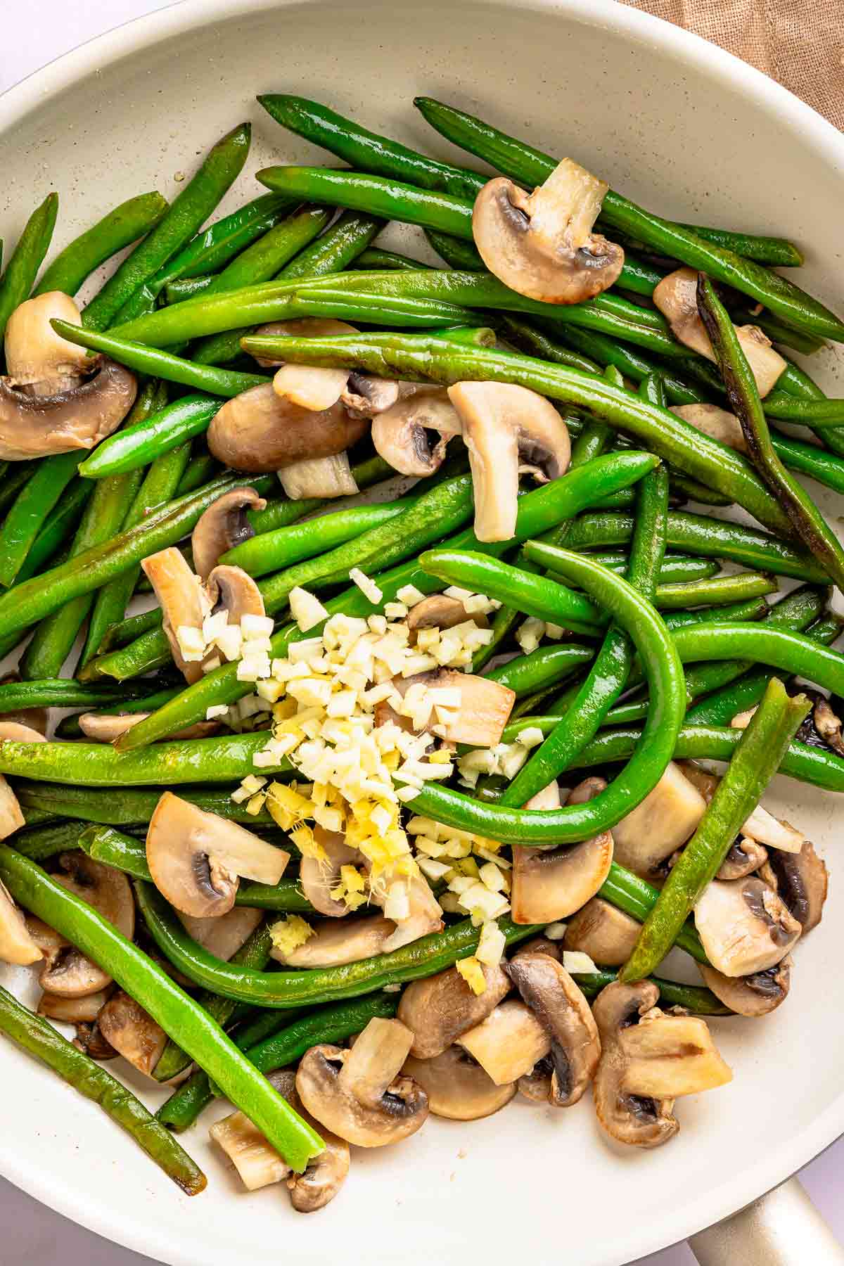 Garlic and ginger cooking with green beans and mushrooms in a skillet