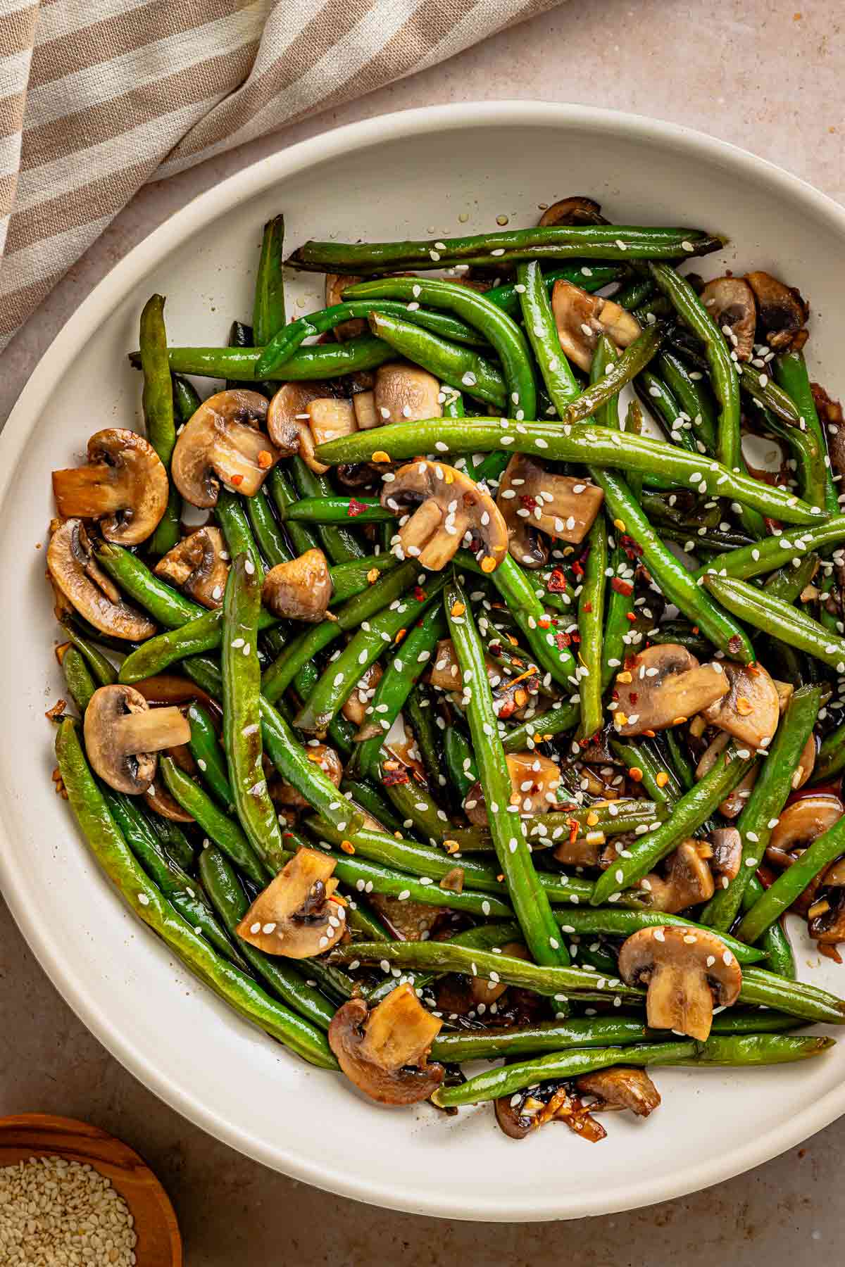 Vegan garlic soy green beans with mushrooms topped with sesame seeds and chili flakes