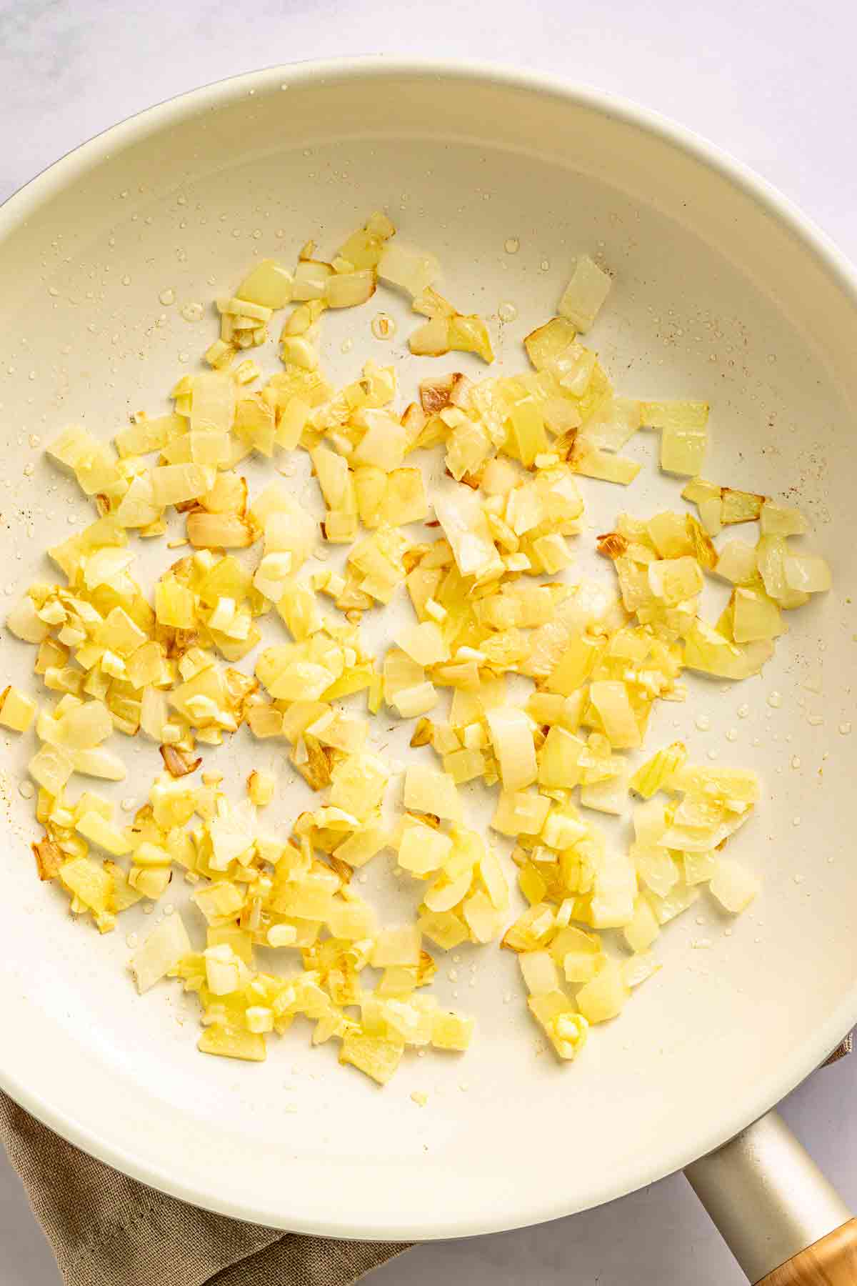 Diced onion and garlic cooking in a white skillet