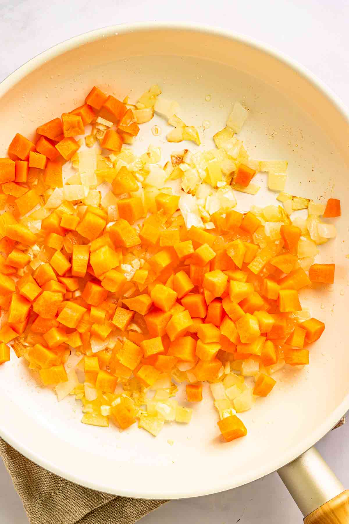 Diced carrots and onions cooking together in a white skillet
