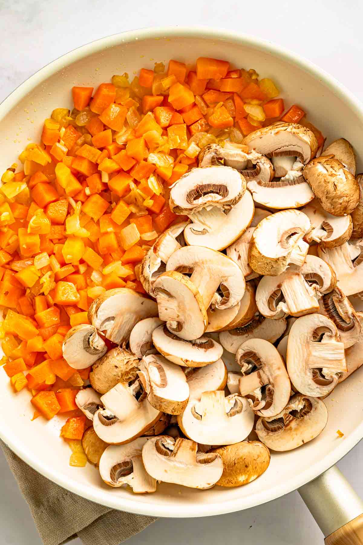Sliced mushrooms added to carrots and onions in a skillet