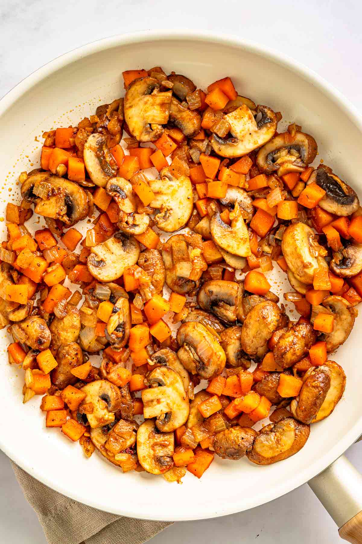 Sautéed mushrooms and carrots browned in a white skillet