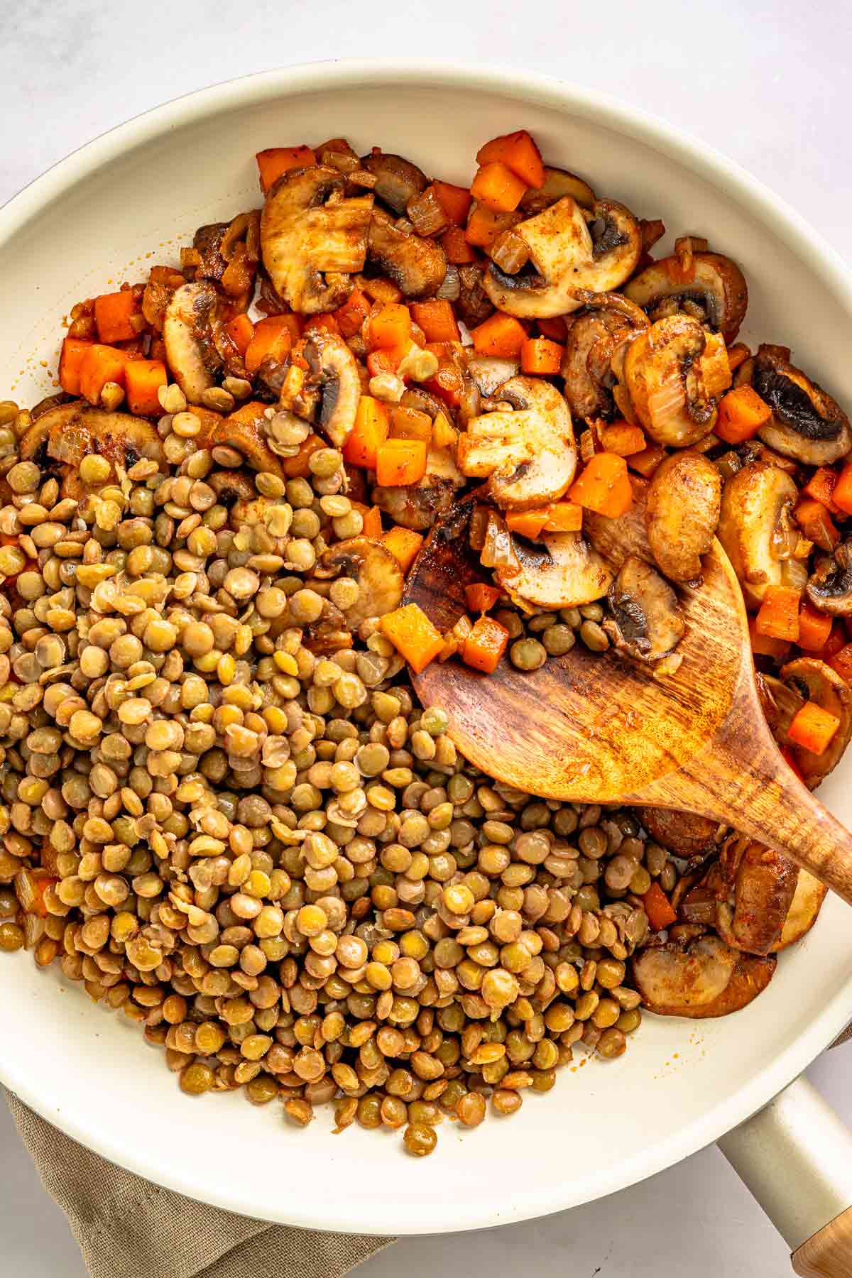 Cooked lentils added to sautéed mushrooms and vegetables in a skillet