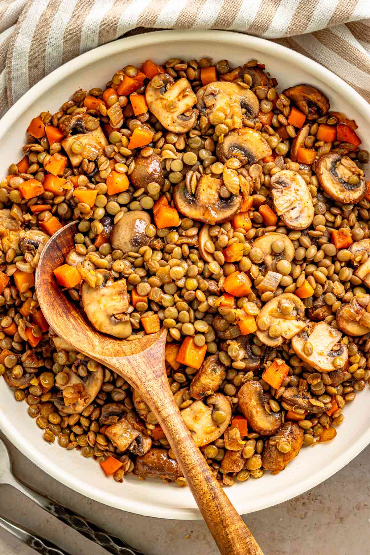 Lentils and sautéed mushrooms with carrots in a white skillet with wooden spoon