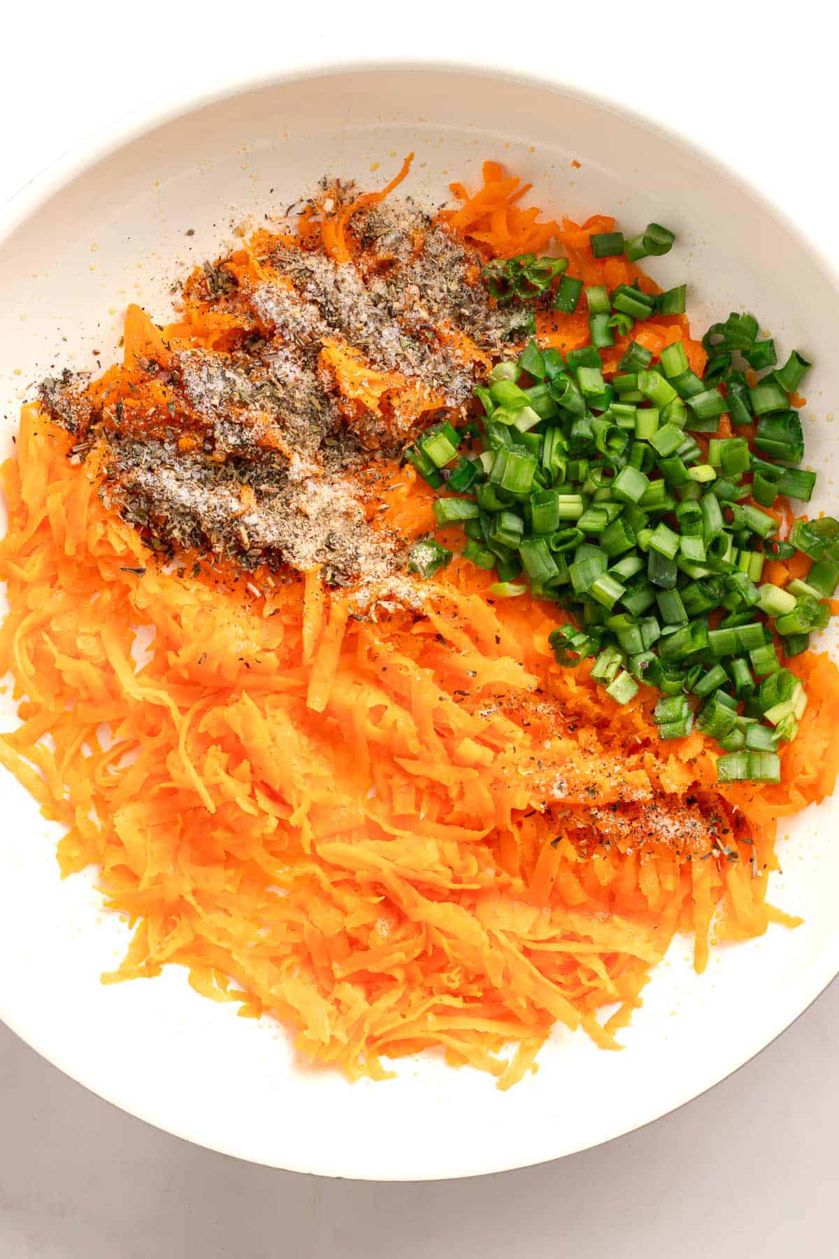 Grated sweet potato with green onions and seasonings in a white bowl