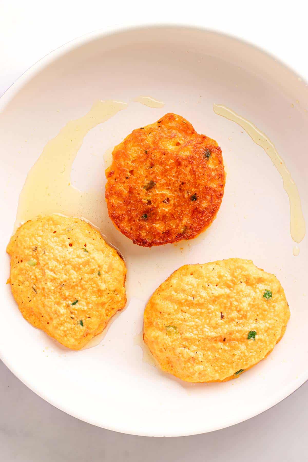 Three lentil fritters cooking in a skillet with golden brown tops