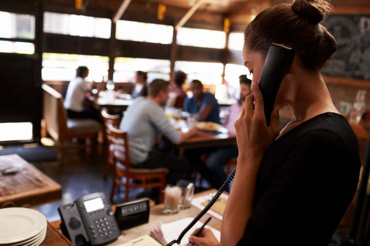 Restaurant staff member taking a phone call while working near the dining area.