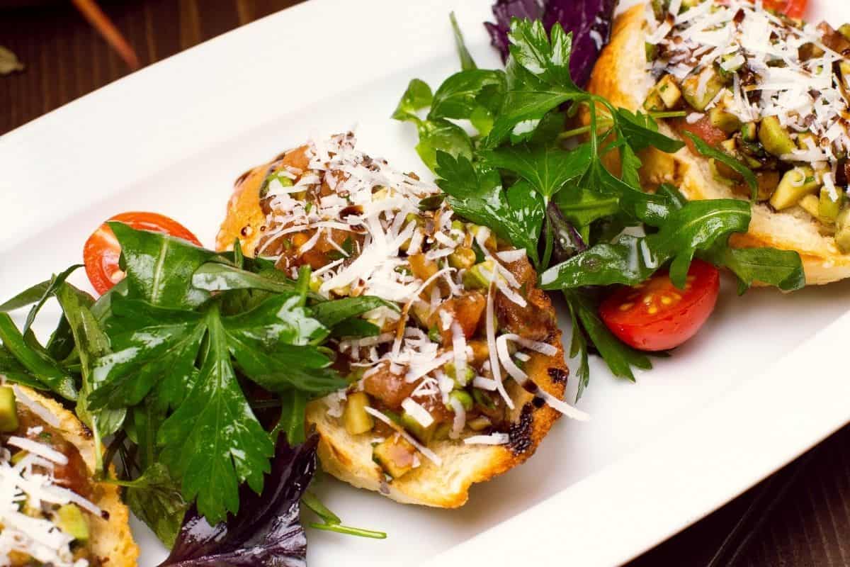 Plate of vegan food topped with fresh herbs, vegetables, and grated cheese alternative.