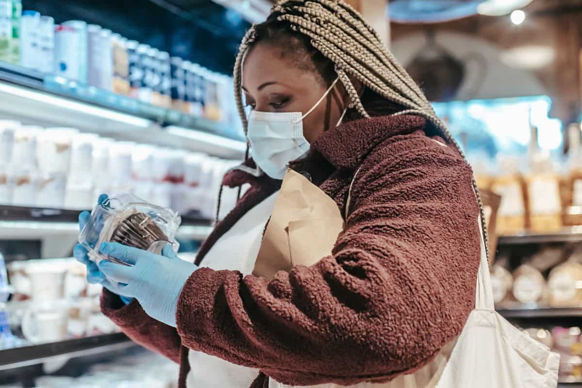 Woman wearing a face mask reading a product label while shopping in a grocery store.