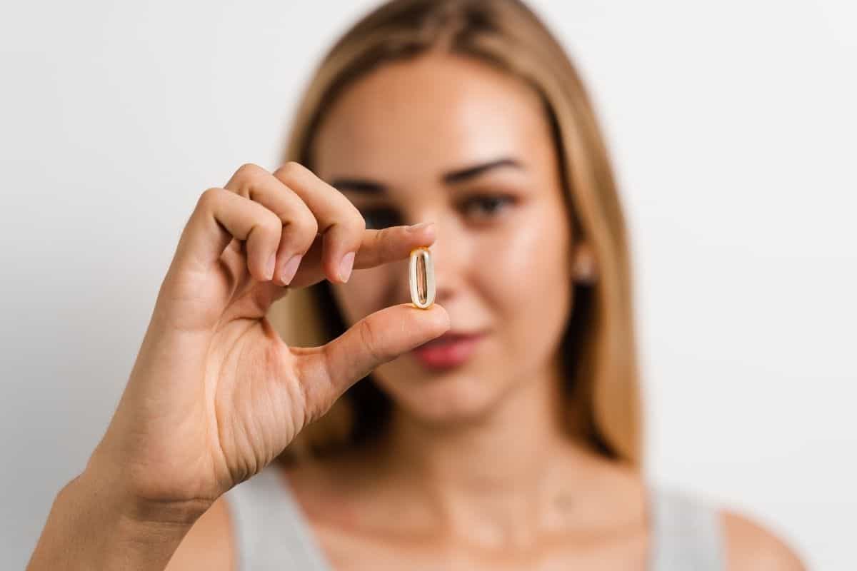Woman holding a single supplement capsule between her fingers.