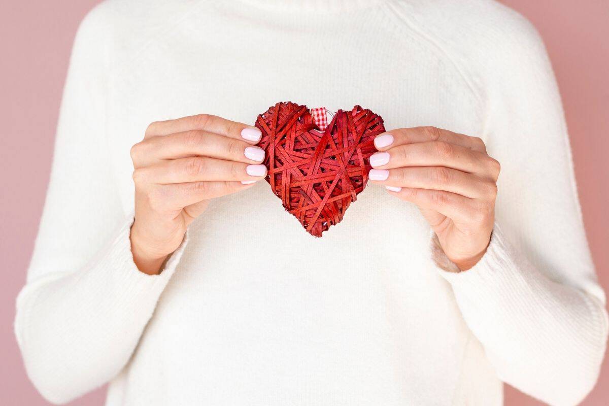 Woman holding a red heart-shaped decoration against her chest on a pink background.