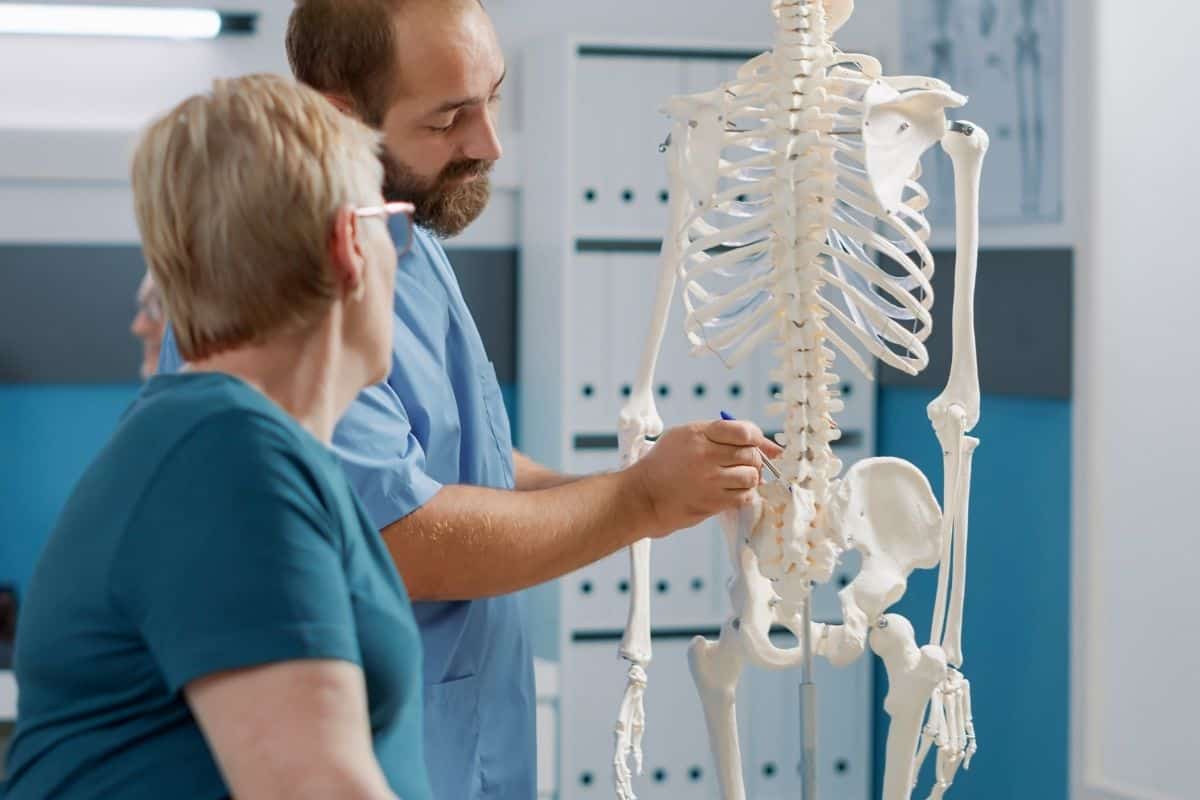 Healthcare professionals discussing a human skeleton model in a clinical setting.