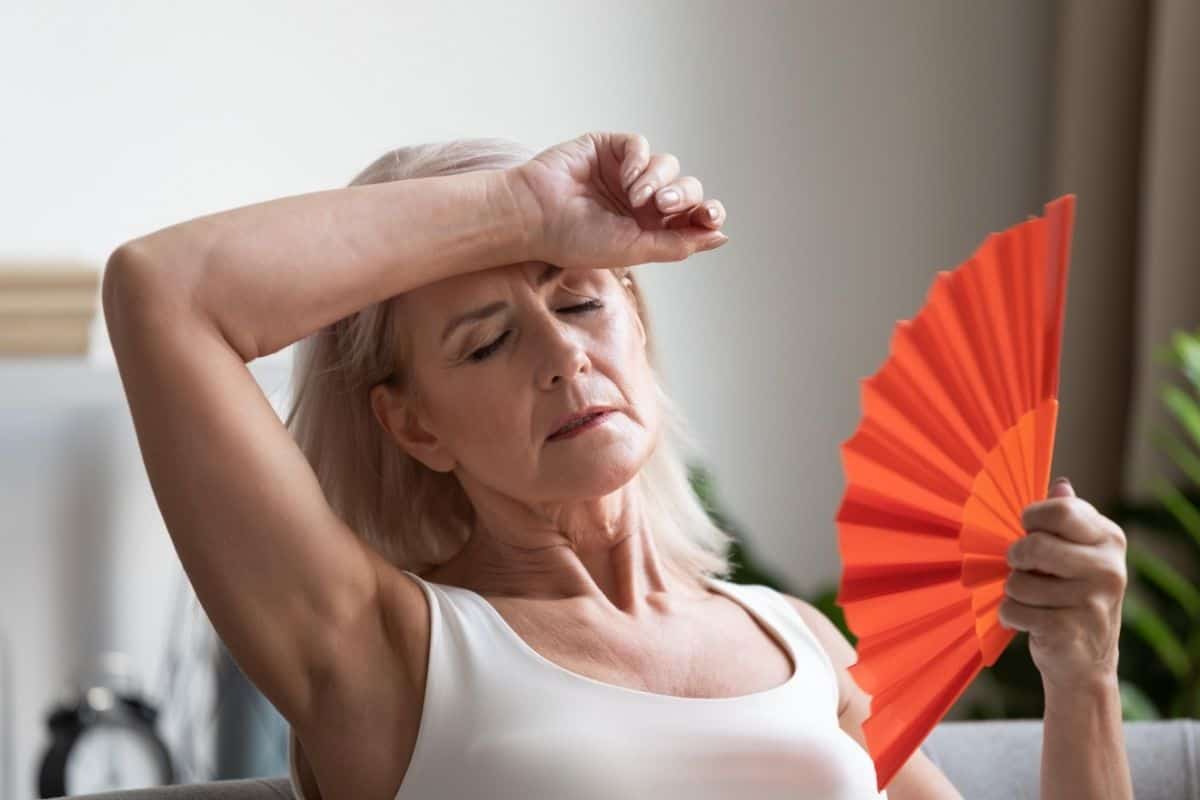 Older woman feeling overheated while cooling herself with a handheld fan.