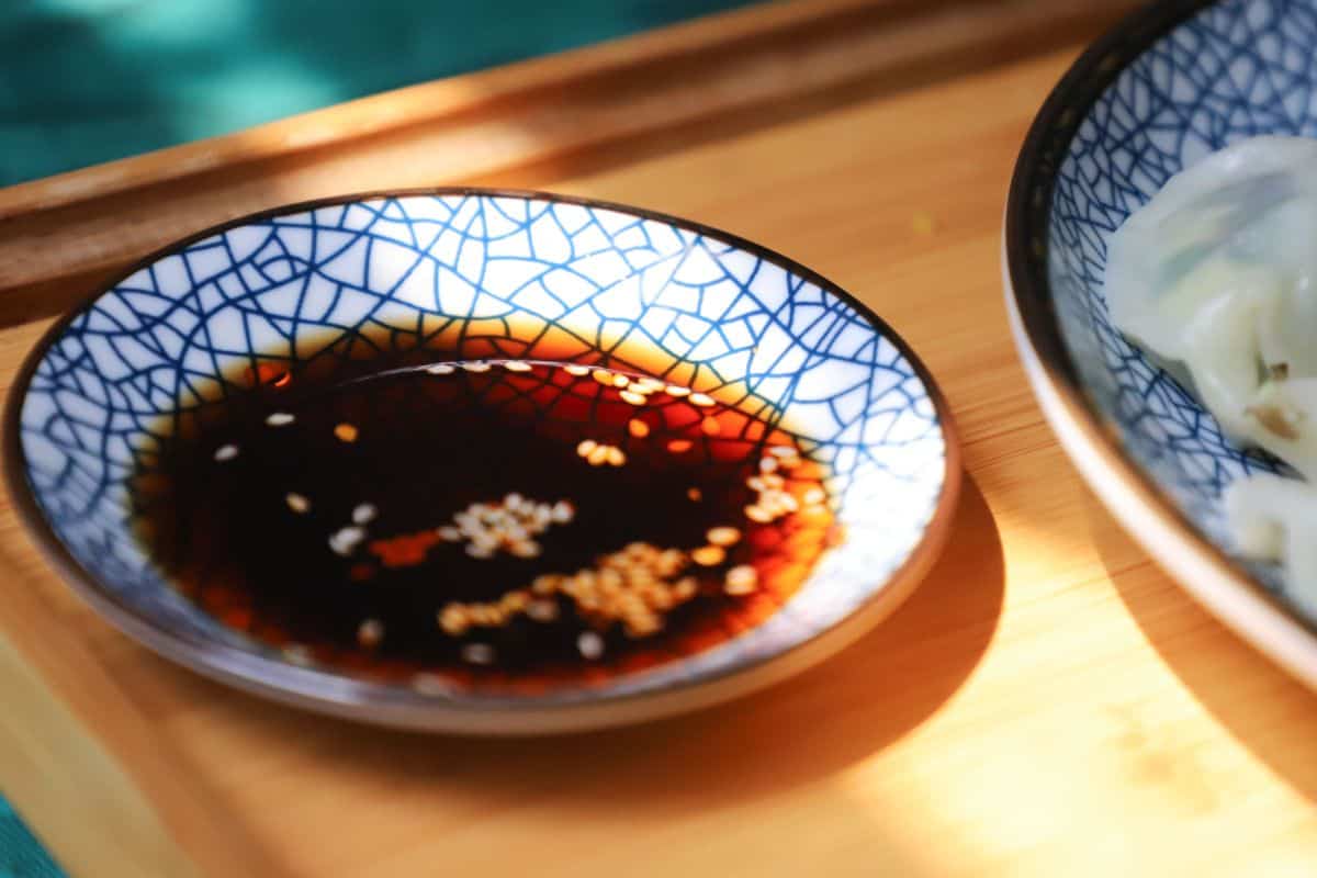 Small bowl of soy sauce topped with sesame seeds.
