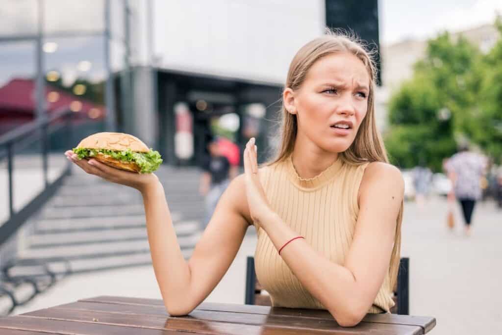 Woman holding a burger and gesturing that she does not want to eat it.