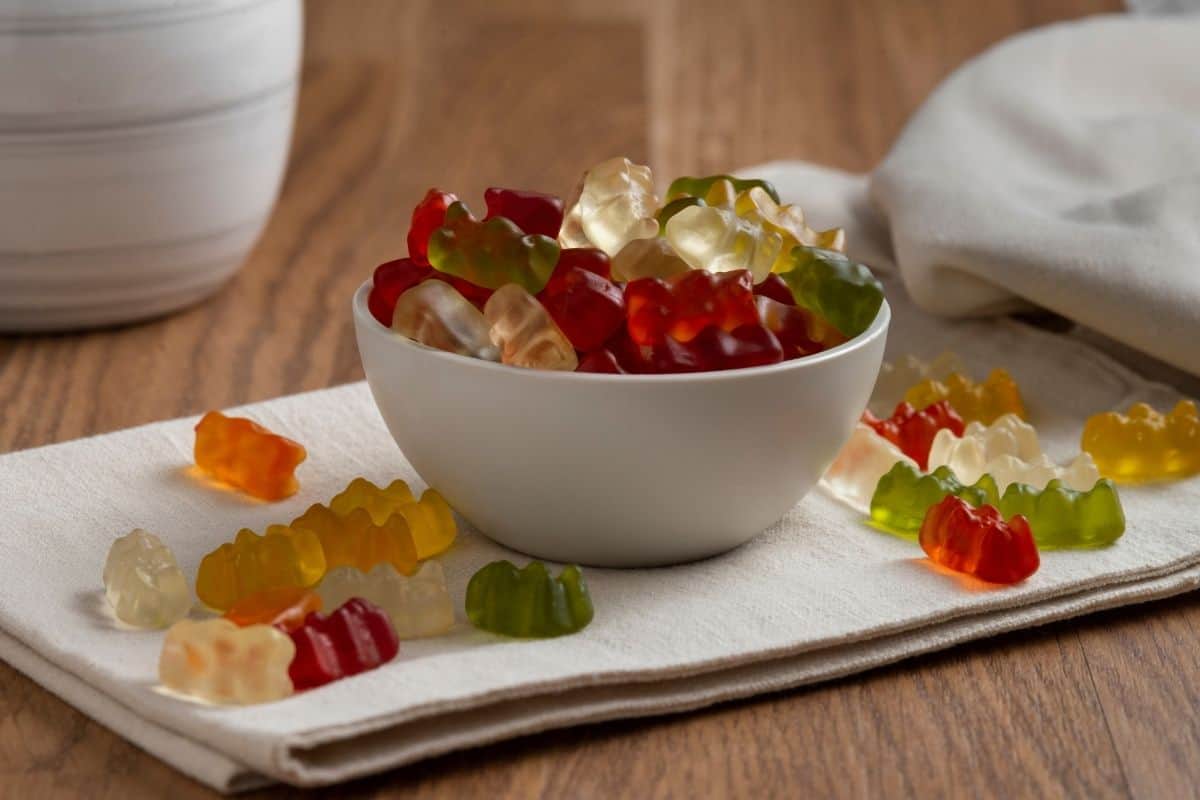 Colorful gummy candies in a white bowl on a wooden table.