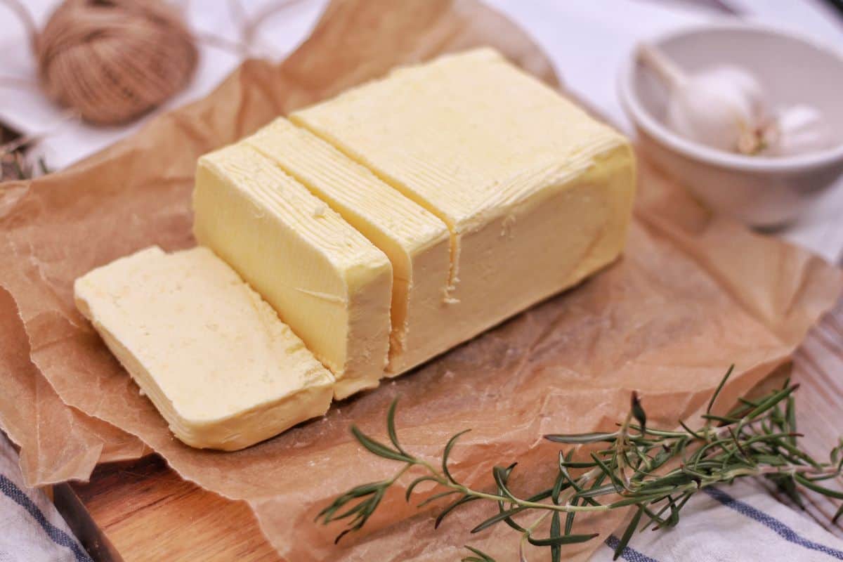 Sliced block of butter on parchment paper with garlic and rosemary.